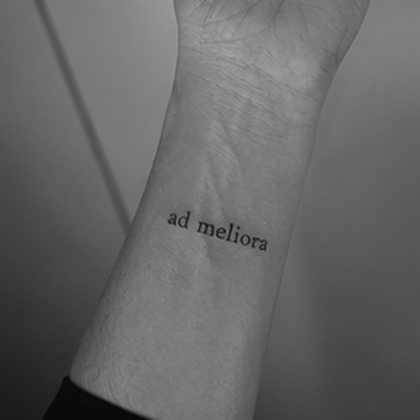 Fine line lettering wrist tattoo reading ad meliora