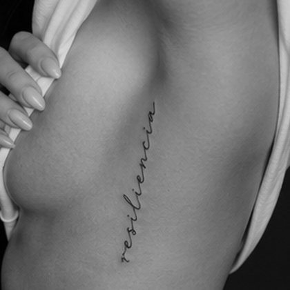 Script lettering rib tattoo reading resiliencia